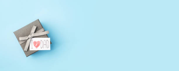 A gray gift box with a Father's Day greeting card on a blue background. Festive banner with copy space.