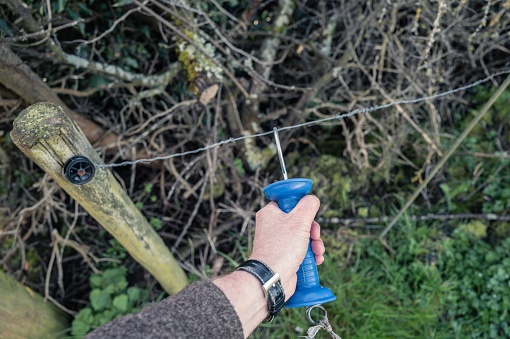 Farmer seen attaching a metal hook to a livestock electric fence. Once hooked, the electric fence is live. Used to keep livestock from escaping the paddock.