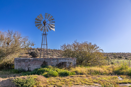 Old and unused metal windmill and dilapidated brick and concrete dam in the Karoo region of South Africa.