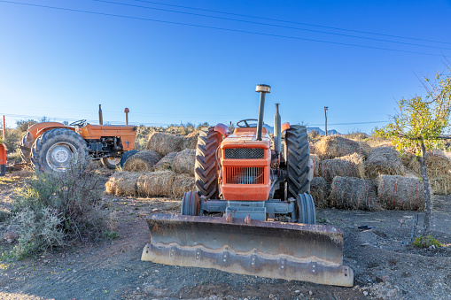 Rural farm landscape with tractors and rolled hay bales stacked behind one of the tractors.