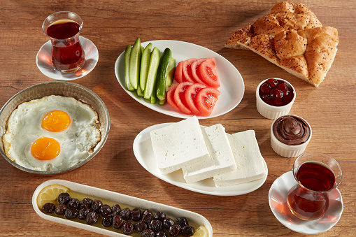 Cheese Plate, tomatoes, cucumber, jam, fried eggs, tea, olives and bread over table