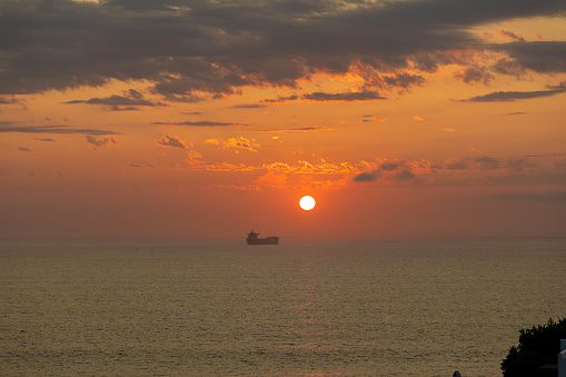 Ship on the ocean during  a glowing sunset with a hot burning sun and clouds in the sky.