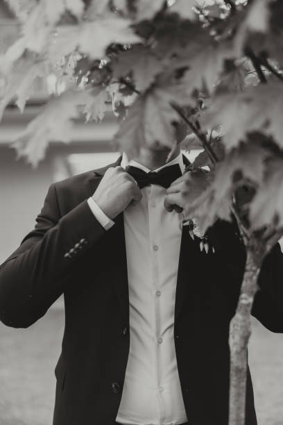 黒いスーツを着た新郎は、緑の木を背景にポーズをとり、ジャケットを調節します。結婚式の白黒の肖像画。 - fashion model personal accessory suit tying ストックフォトと画像