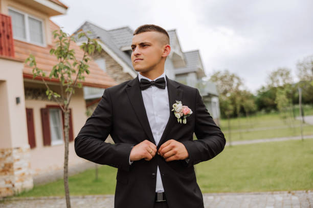 the groom in a black suit adjusts his jacket, poses against the background of a green tree. wedding portrait. - fashion model personal accessory suit tying ストックフォトと画像