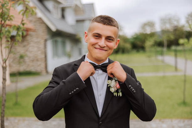 the groom in a black suit adjusts his bow tie, poses against the background of a green tree. wedding portrait. - fashion model personal accessory suit tying ストックフォトと画像