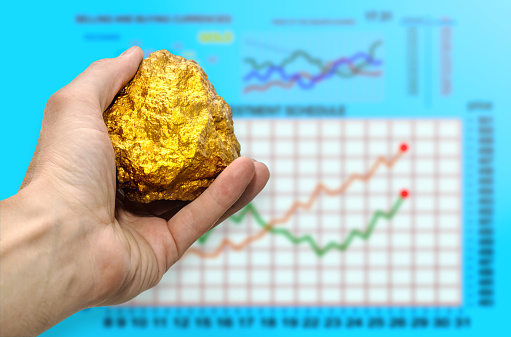 Gold nugget in a manâs hand against the backdrop of rising stock prices. Stock Exchange. Concept of wealth and success in the financial sector. Treasures, investments.