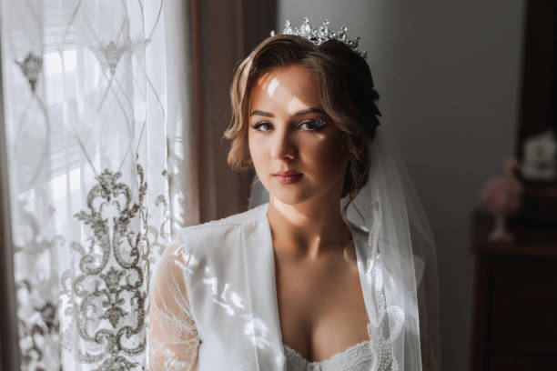 istock A beautiful brunette bride with a tiara in her hair is getting ready for the wedding in a beautiful robe in boudoir style. Close-up wedding portrait, photo. 2112059164