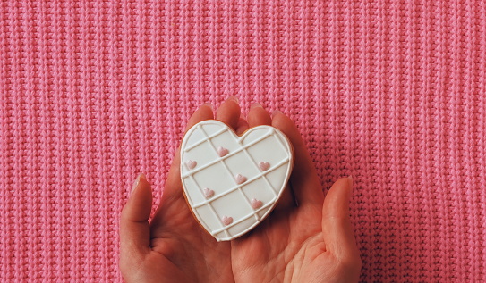 A Gentle Touch of Sweetness. Hand Presenting a Heart-Shaped Cookie on a Pink Knitted Texture. Top View