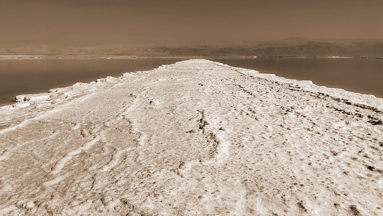 Sepia Tone Salt Formation Leading Into Vast Water Body Against Mountain Range