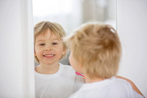 Cute toddler child, blond boy, brushing his teeth at home, isolated
