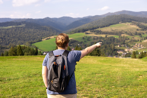 Men pointing finger on mountains background. Young male with backpack hiking in nature. Back view