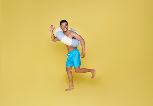 Full body young tourist asian man hold inflatable ring running happy summer vacation isolated on yellow background.