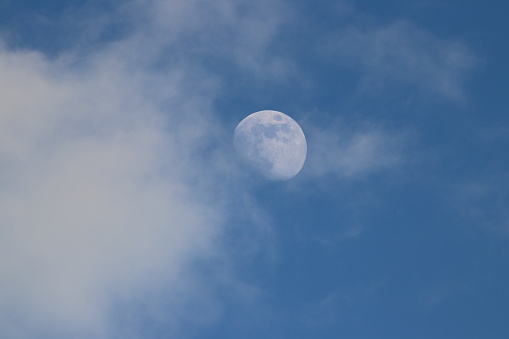 Full moon and fluffy white clouds in blue sky