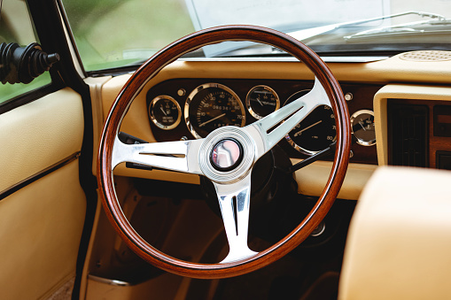 Wooden steering wheel with retro vintage dashbord of oldtimer. Luxurious car equipment in an elegant and old fashion style.