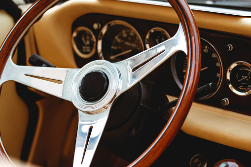 Wooden steering wheel with retro vintage dashbord of oldtimer. Luxurious car equipment in an elegant and old fashion style.