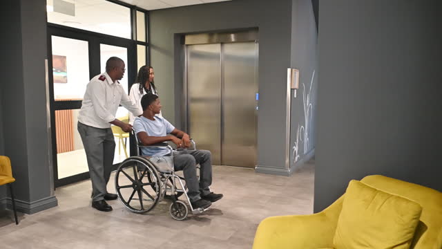 Deaf patient being pushed in wheelchair by male nurse and female doctor waiting at elevator in hospital