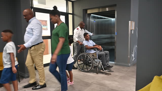 Deaf patient being pushed in wheelchair by male nurse and female doctor into elevator in hospital