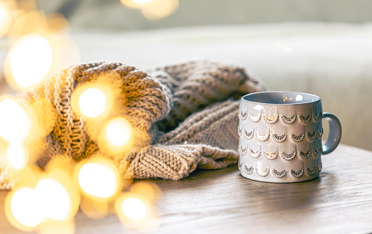 Cozy background with shiny gray cup, bokeh lights and knitted element on wooden background. Copy space.