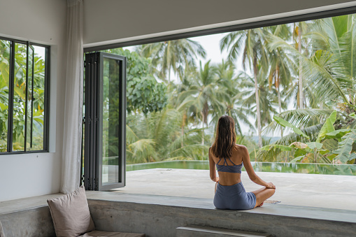 Young woman relaxes in outdoor living room with jungle in distance, performs yoga exercises