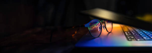 istock Glasses lie on the laptop, reflecting light from the screen in the dark. 2112247132