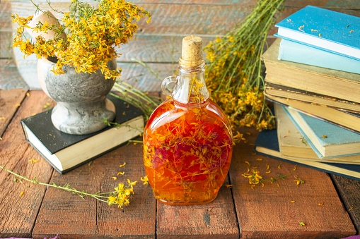 Vintage books, dried St. John's wort flowers and bottles of St. John's wort oil on a wooden background.