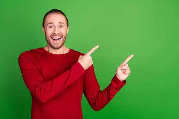istock Photo of impressed funky man with stubble dressed red pullover indicating at proposition empty space isolated on green color background 2112260044