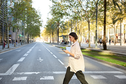 A businesswoman in casual attire is captured walking and using her smartphone, reflecting the dynamic nature of modern urban professionals