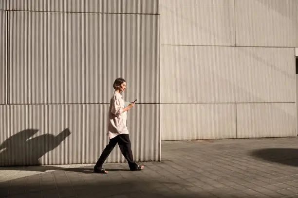 Busy confident businesswoman walking the city street while using a mobile phone in the sunset light Busy confident businesswoman walking the city street while using a mobile phone in the sunset light