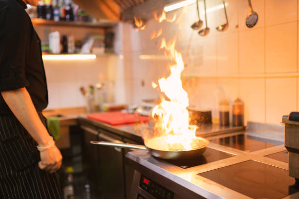 Chef uses flambe culinary technique cooking piece of meat in restaurant. Flame in frying pan under control of experienced cook