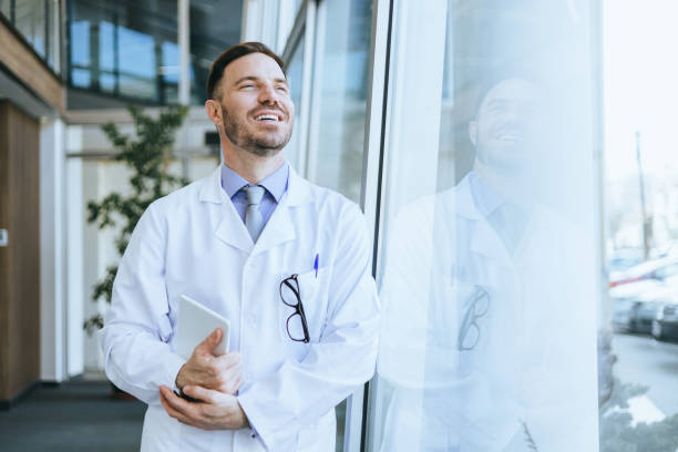 istock Happy male doctor with digital tablet by window 2112296309