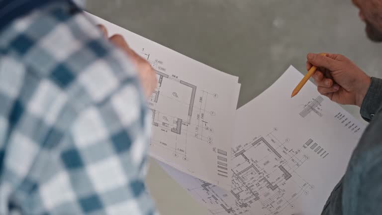 An engineer and a builder discuss a house project based on detailed drawings. Work on a construction site. Developer