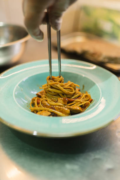 istock Chef twists noodles around metal chopsticks serving dish 2112318356