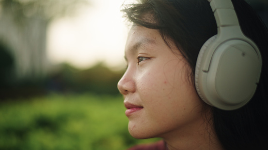 Asian teenage girl relax listening while wearing headphones at green environment.