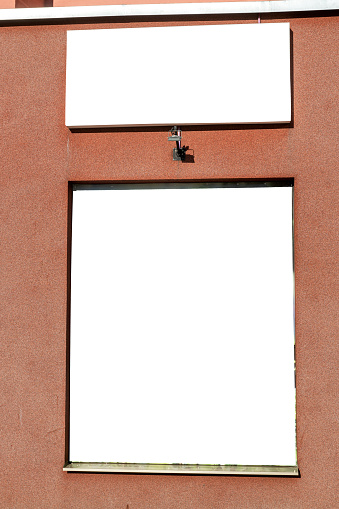 Blank banner in the window on the facade of a red building outdoors. Billboard design. Billboard in the building window