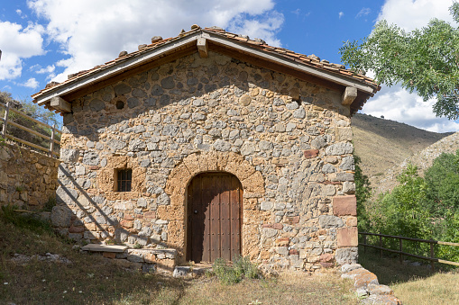 A quaint stone structure featuring a wooden door and a window, this building is nestled within a grassy expanse. It is known as the Hermitage of La So