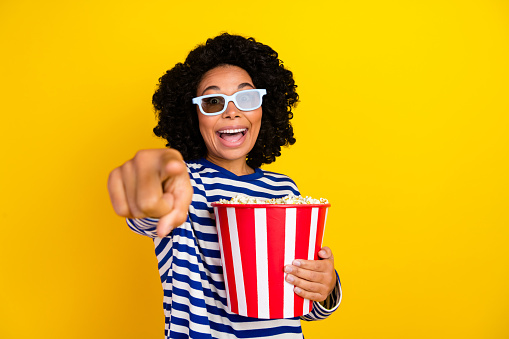 Photo of impressed ecstatic woman dressed striped pullover in 3d glasses hold popcorn directing at you isolated on yellow color background.