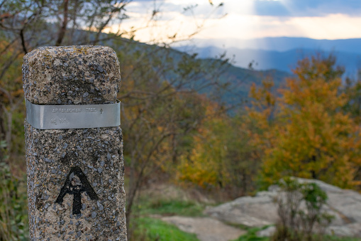 Appalachian trailhead marker in Shenandoah National Park, Virginia. Fall foliage and a sunset can be seen in the background.