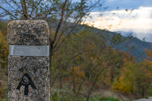 Appalachian trailhead marker in Shenandoah National Park, Virginia. Fall foliage and a sunset can be seen in the background.