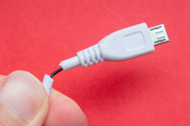 Hand holding damaged charger cable, closeup photo. Isolated on red background.