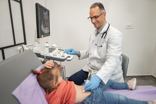 Male pediatrician examining little girl with ultrasound at the medical clinic.