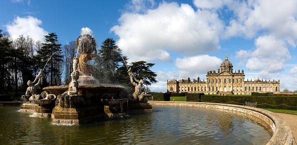 Castle Howard, York, UK - March 23, 2024.  A landscape panorama of The Atlas Fountain in the formal gardens of Castle Howard Stately House in the Howardian Hills with sunshine and blue sky