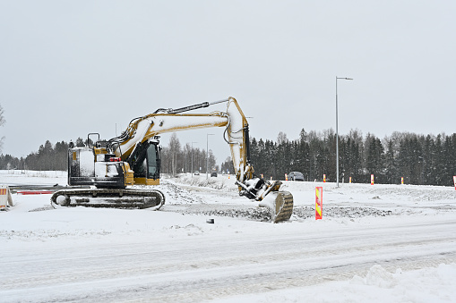 An excavator works amidst a snowy landscape, clearing snow or engaged in construction