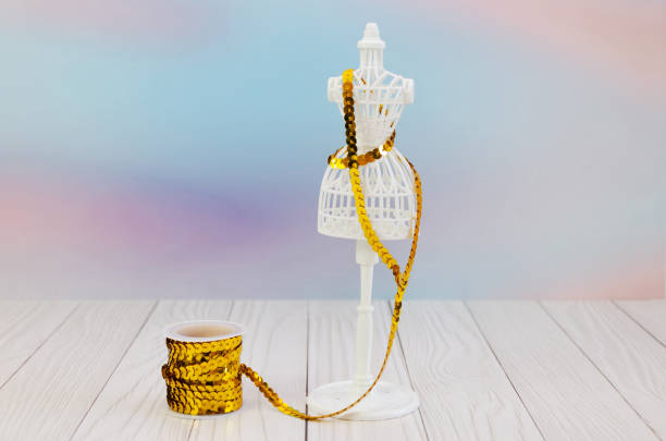 spool of shiny braid with sequins and a miniature mannequin on a lilac background. Concept: needlework, sewing, handmade