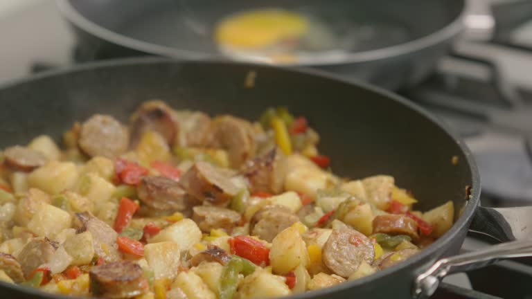 A breakfast hash of sausages, peppers, onions and potatoes simmers in a cast iron skillet.