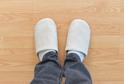 Closeup of a man wearing a new pair of slippers on a hardwood floor.