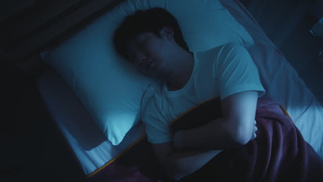 Young Man Sleeping Cozily on a Bed in His Bedroom at Night