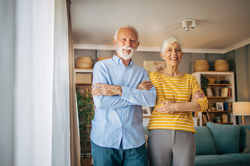 Elderly beautiful couple standing together with folded hands in the living room