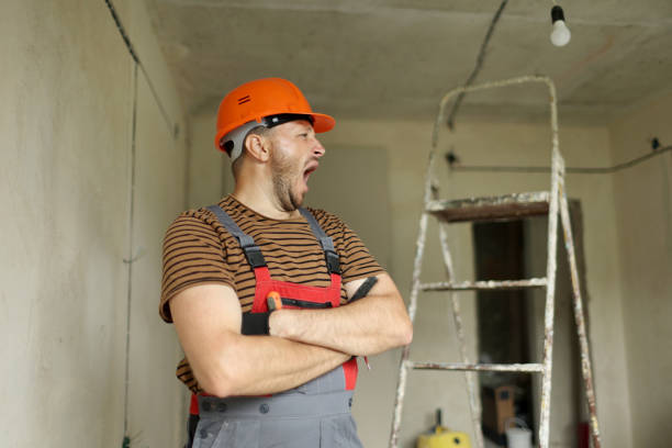 A construction worker in a yellow hard hat is carefully measuring with a tape measure, showcasing his work attire