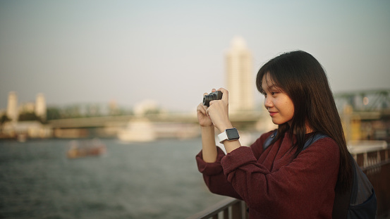 Asian girl taking a photo of view while traveling by the river.