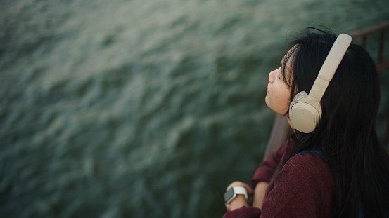 Contemporary art collage, modern surreal design of young woman listening music in headphones isolated over blue background. Music enjoyment. Concept of art, music, creativity, vintage style and ad.